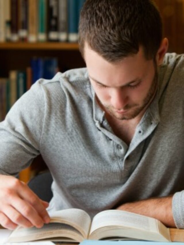 Male student researching with a book in a library